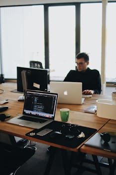 Man in Black Shirt Sits Behind Desk With Computers